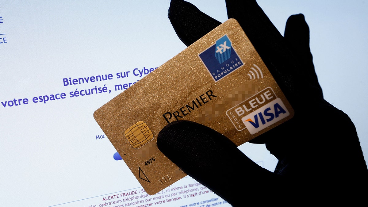 A picture shows a person holding a Visa Premier credit card in front of a computer screen displaying an internet website which bears a warning message against fraud .