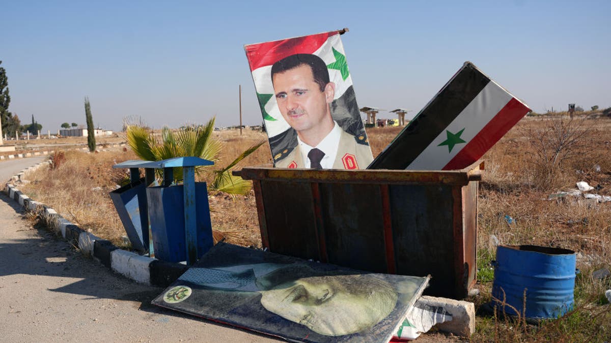 TOPSHOT - A picture taken at the entrance of the Kweyris military airfield in the eastern part of Aleppo province on December 3, 2024 shows a portrait of Syria's President Bashar al-Assad and a national flag in the garbage dumpster following the take over of the area by rebel groups. A war monitor on December 1 said Ankara-backed groups seized control of the towns of Safireh and Khanasser southeast of Aleppo from government forces, and also took the Kweyris military airport.
