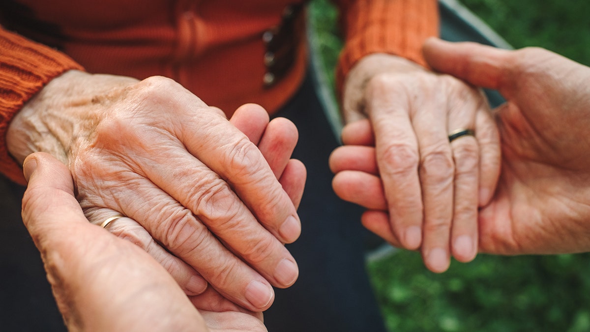 Two pairs of hands in frame, one on top of the other. The subjects are holding hands, both elderly in appearance.