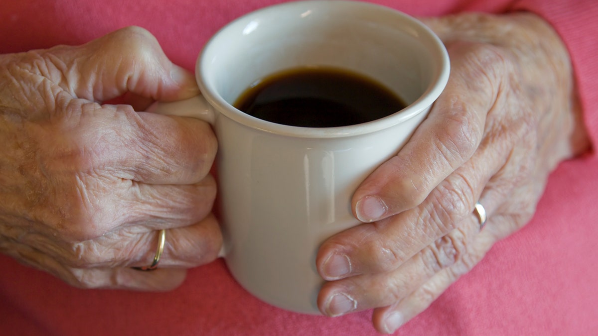 An elderly woman's hands hold a cup of coffee.