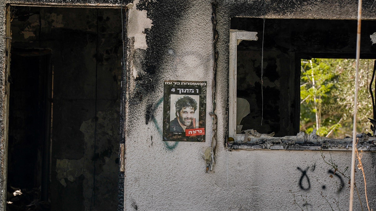 Charred wall of a burned home in Nir Oz with a poster of a murdered Israeli man