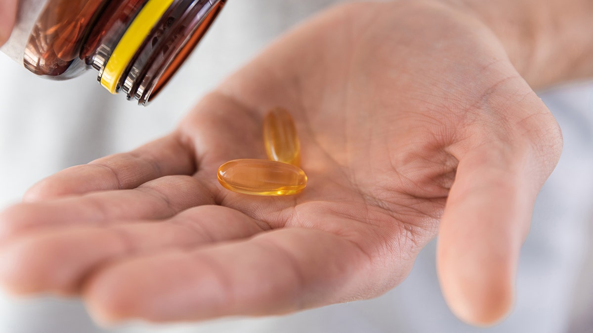 Man pouring fish oil capsules with omega 3, vitamin D in hand from medicine bottle. Nutritional supplement. Health support and treatment concept. Close up: used in piece about vitamin d being able to protect telomeres and support longer living