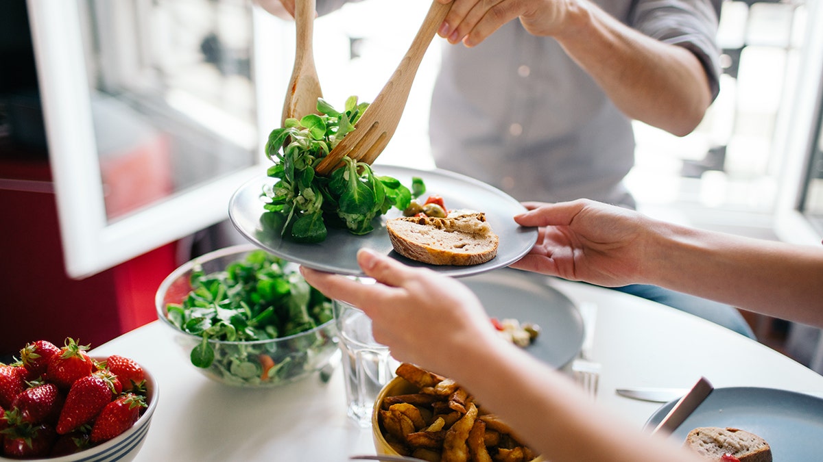 Serving salad for lunch onto a plate with protein