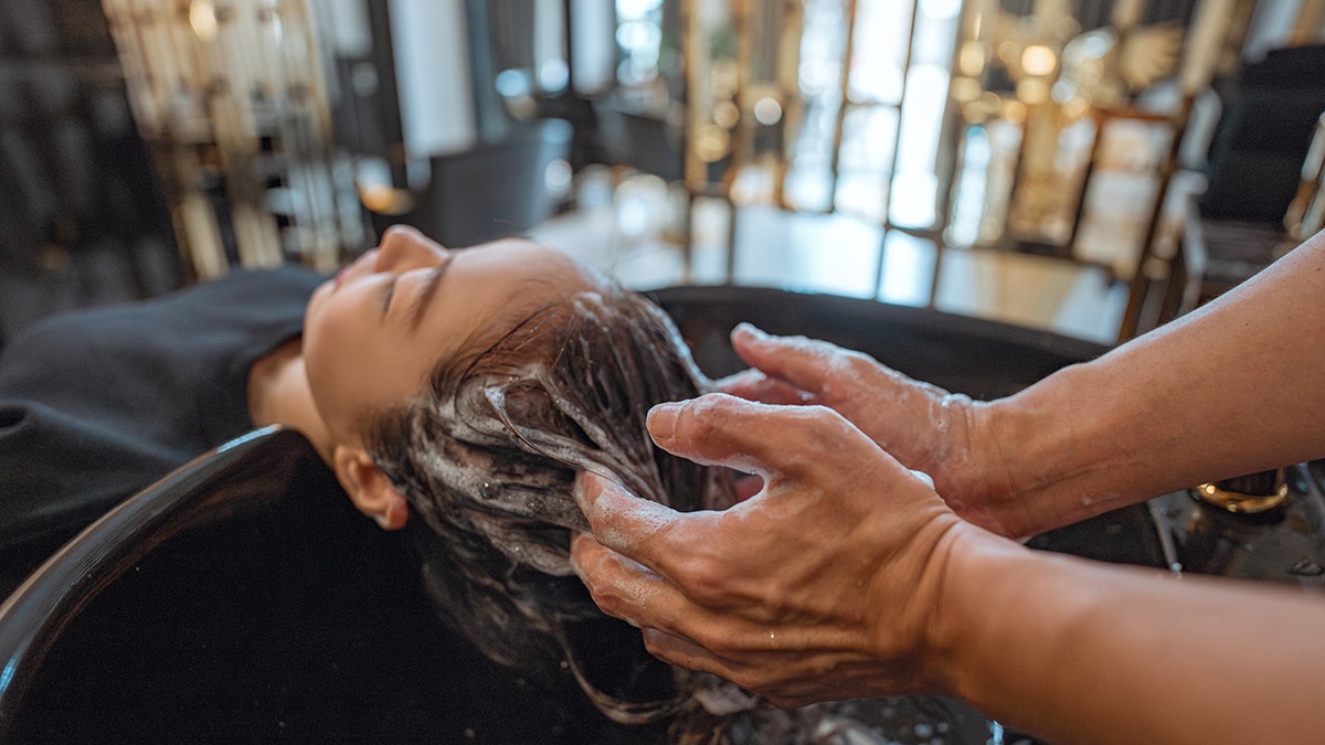Woman lying down on salon washing bed getting hair washed in hair salon by stylist
