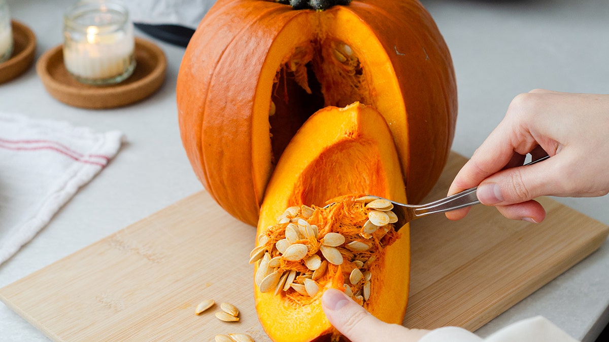 Hand removing seeds from cut pumpkin with spoon