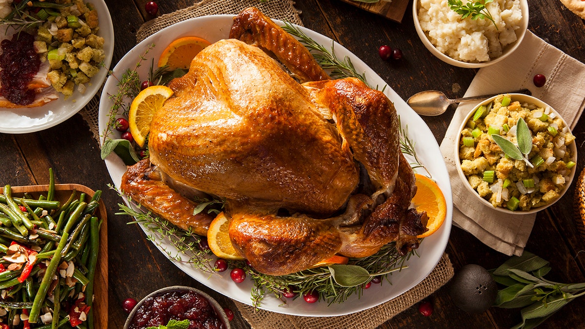 A roasted Thanksgiving turkey surrounded by side dishes including stuffing, mashed potatoes, green beans, and cranberry sauce.