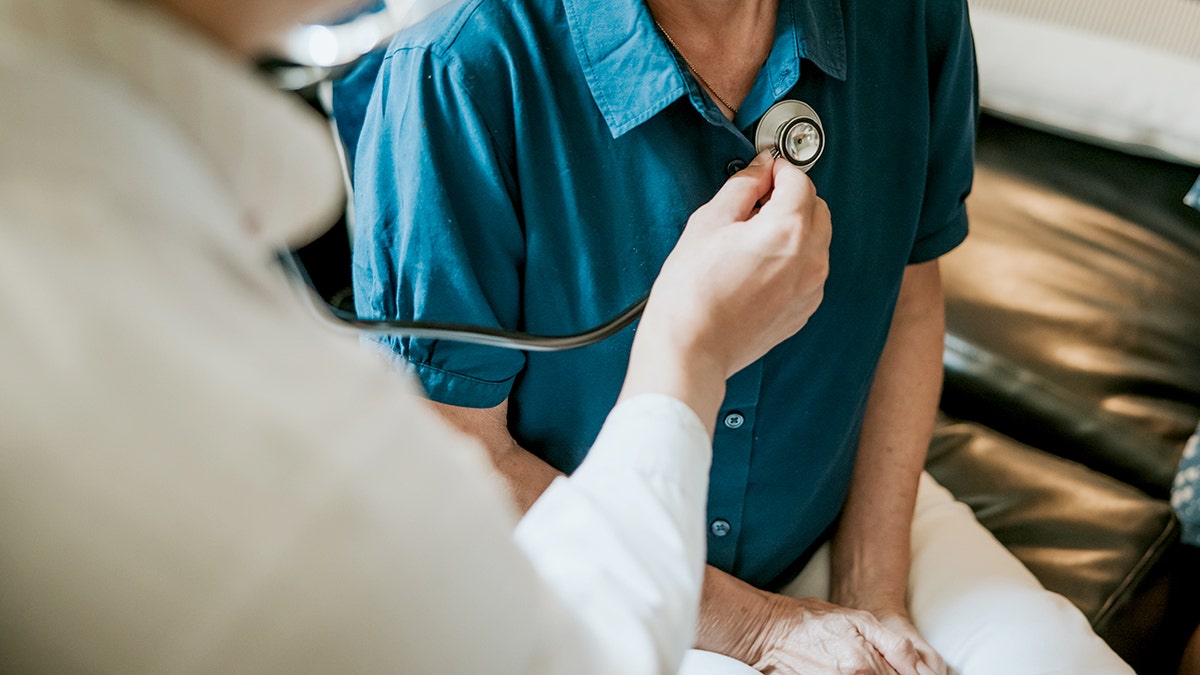 Doctor using a stethoscope to examining senior woman's lung and heartbeat during a healthcare home visit.