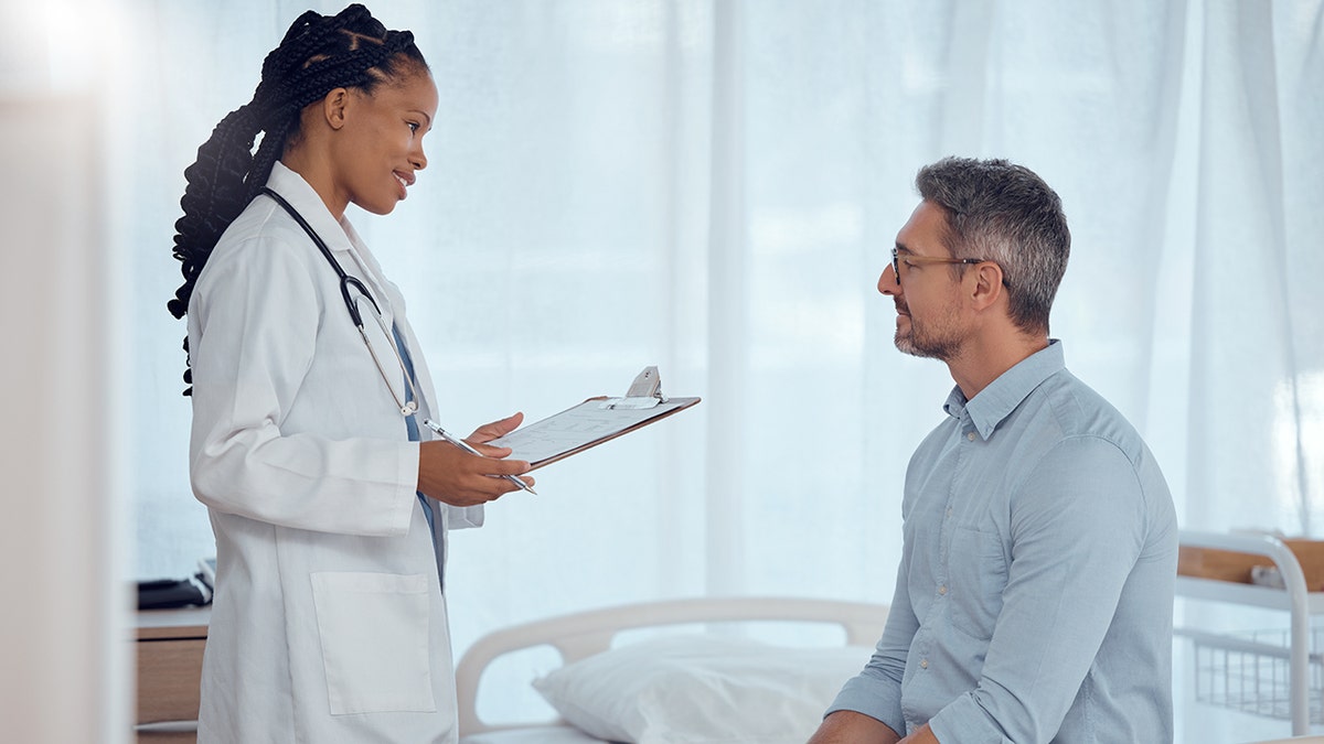 Man sitting across from a female doctor during a medical consultation in an office setting.