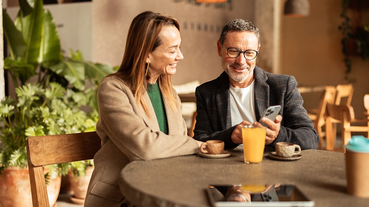 Middle-aged couple sitting at a café table, smiling and sharing a moment together, showing how social connection supports relationships and well-being.
