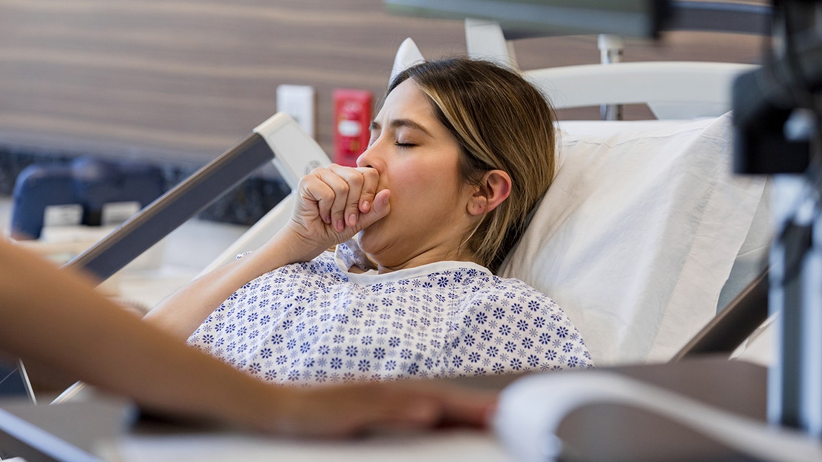 female patient coughs in hospital bed dressed in gown
