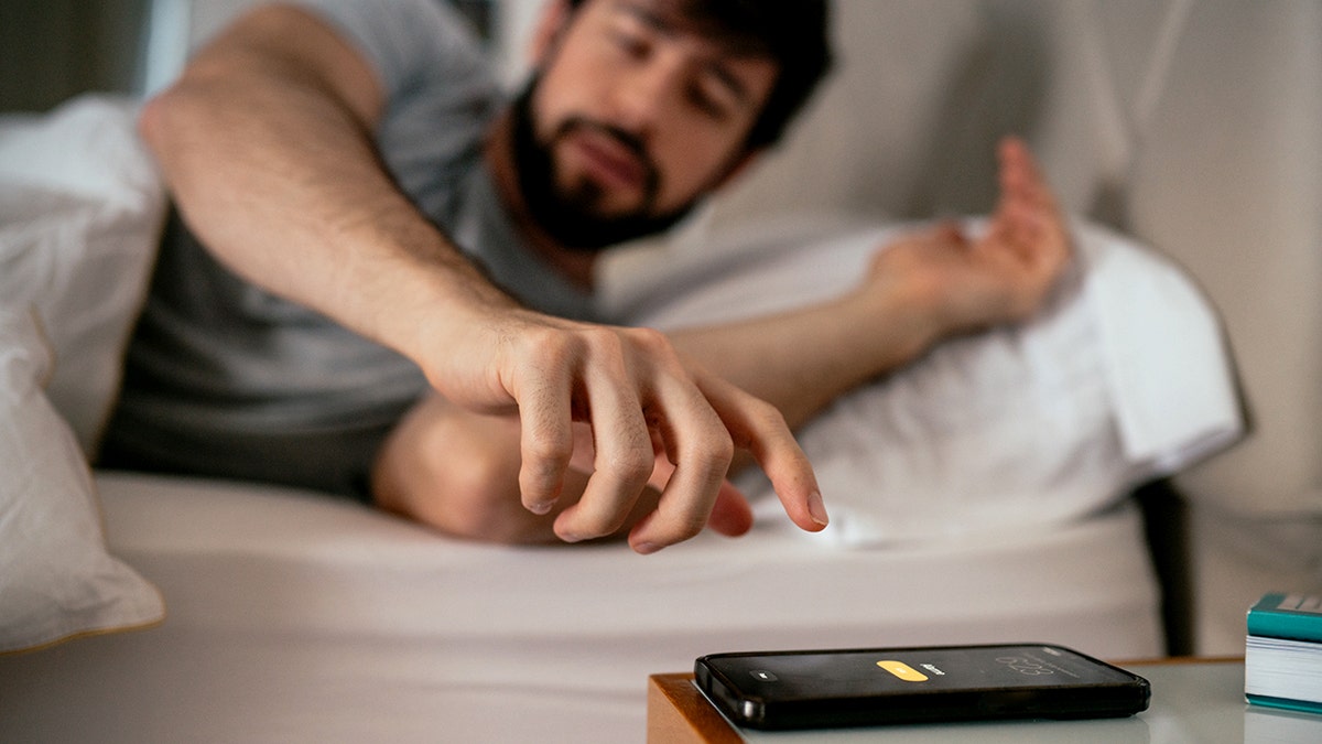 Man waking up on his bed turning off the mobile phone alarm