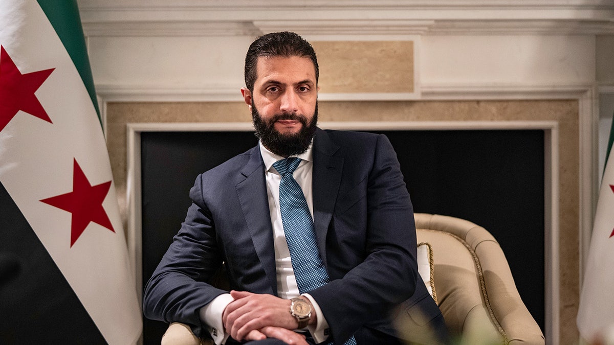 Syrian leader Ahmed al-Sharaa sitting in a chair with his hands folded.