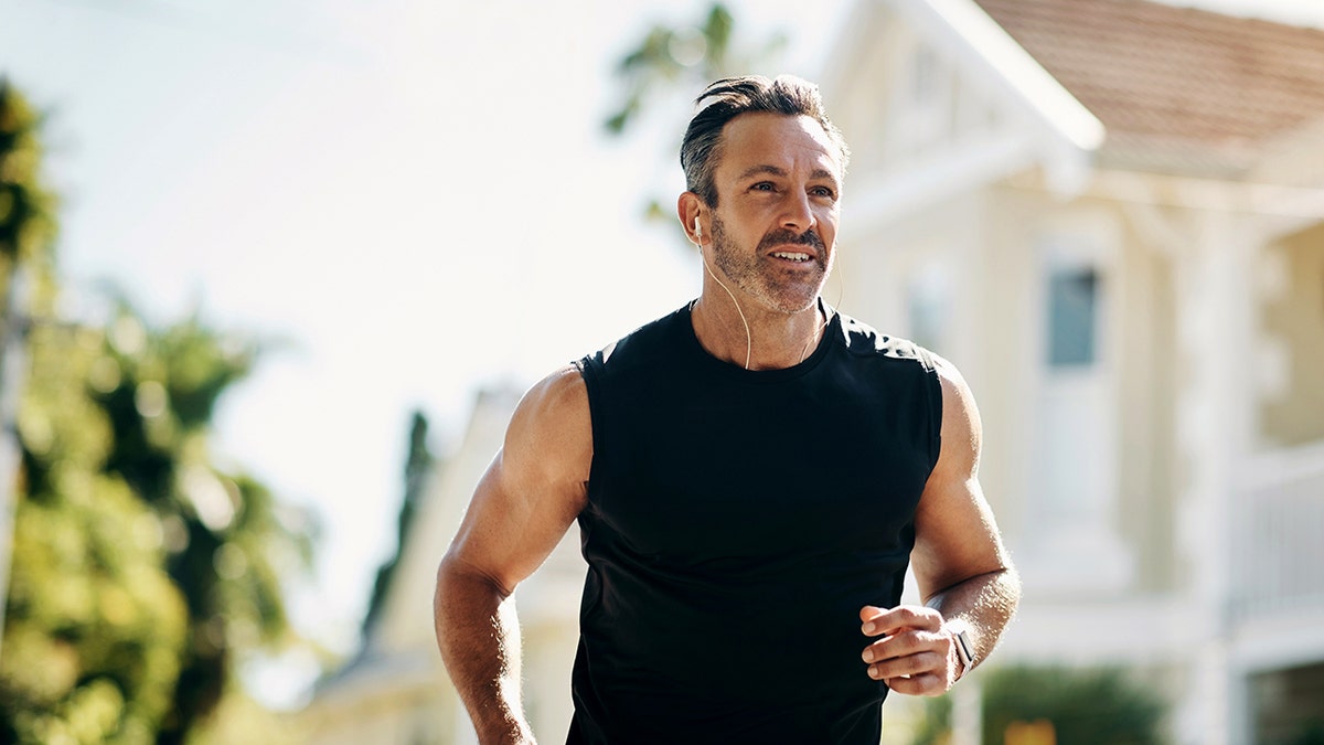 Runner, fitness and senior man running, listening to music outdoor in neighborhood for workout wellness, energy and healthy lifestyle motivation. Sports person with exercise training goal in street