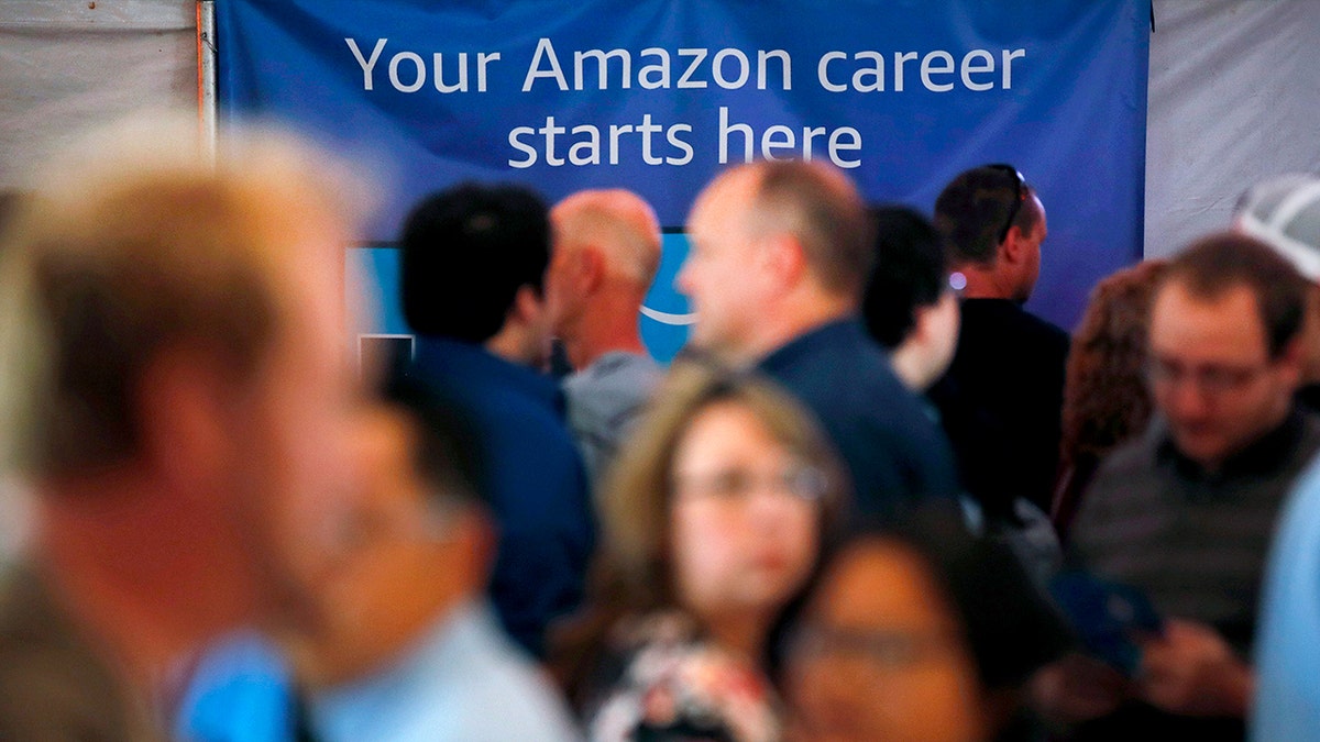 Jobseekers stand in front of a sign that reads, "Your Amazon career starts here."