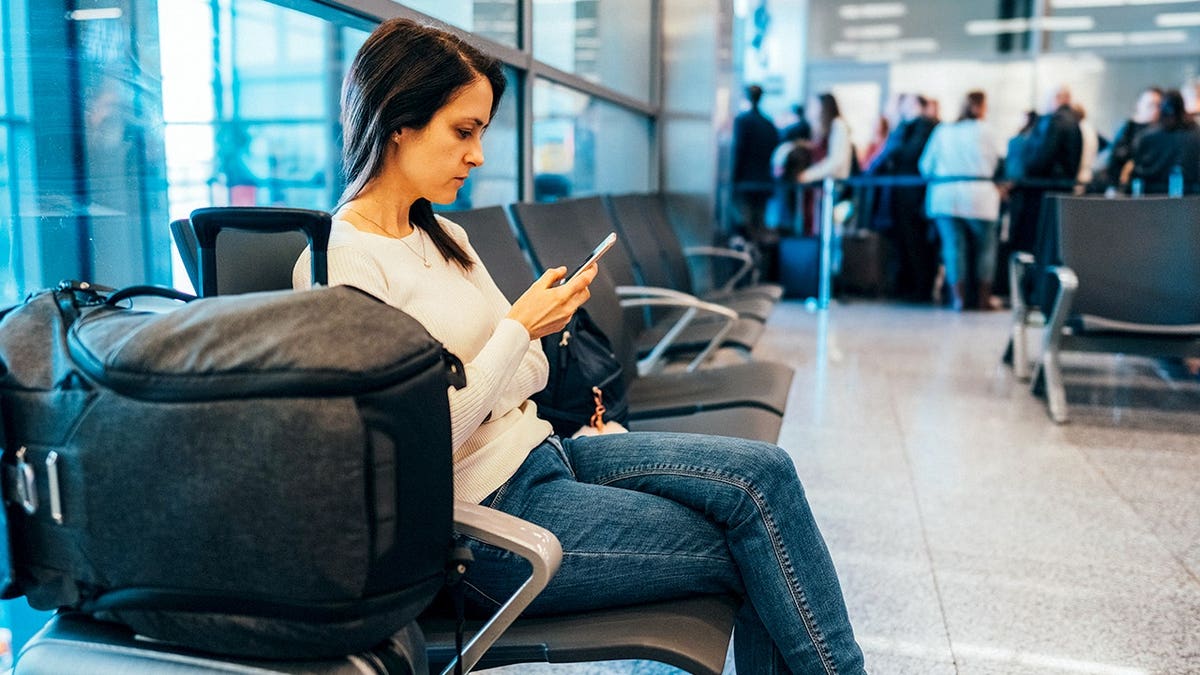 A woman with luggage looks at her phone.