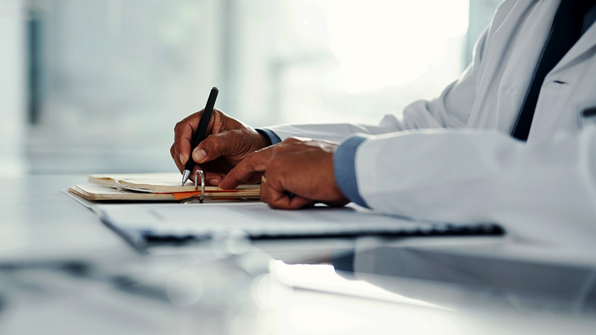 A person in a labcoat writes on a notepad.
