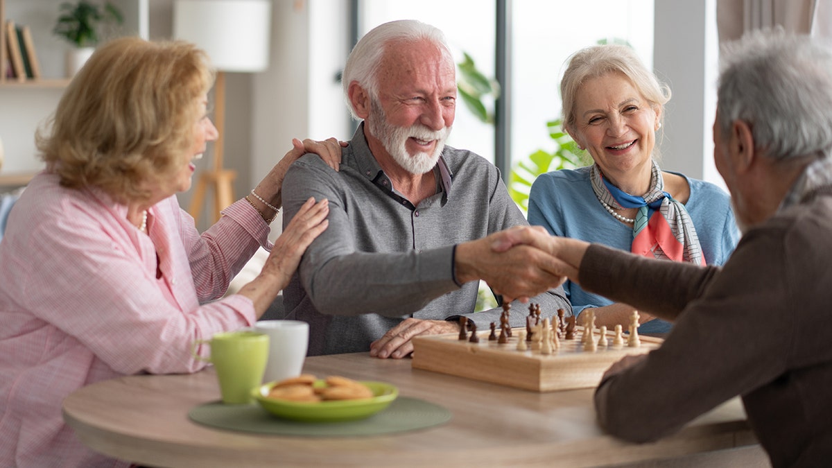 A group of senior friends playing chess together in a room with plants