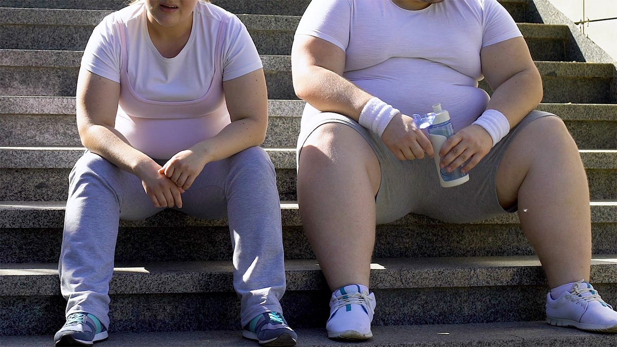 Chubby man and woman resting after hard workout on stairs, breathing heavily