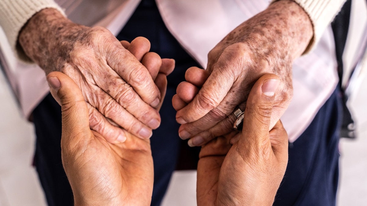 A caregiver holding hands with a senior woman patient.