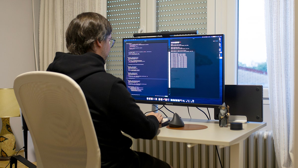 A man sitting in front of a desktop computer displaying code on the monitor.
