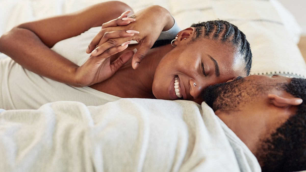 A young woman snuggling into the chest of a man in bed.