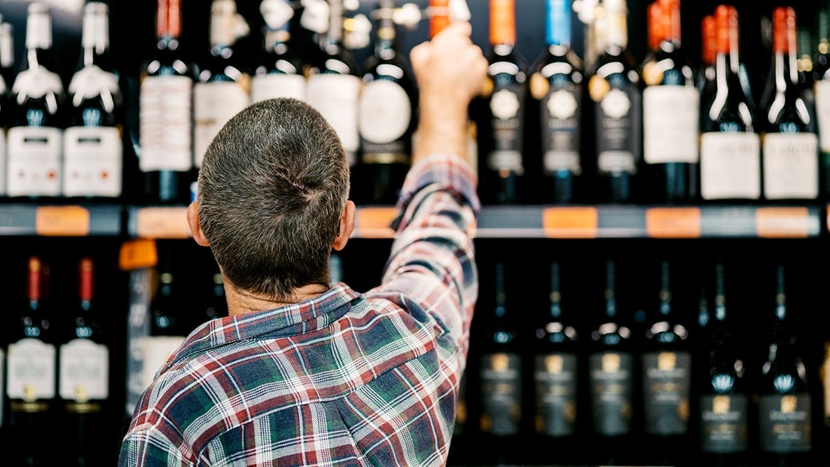 Man reaches for a wine bottle in a liquor store aisle.