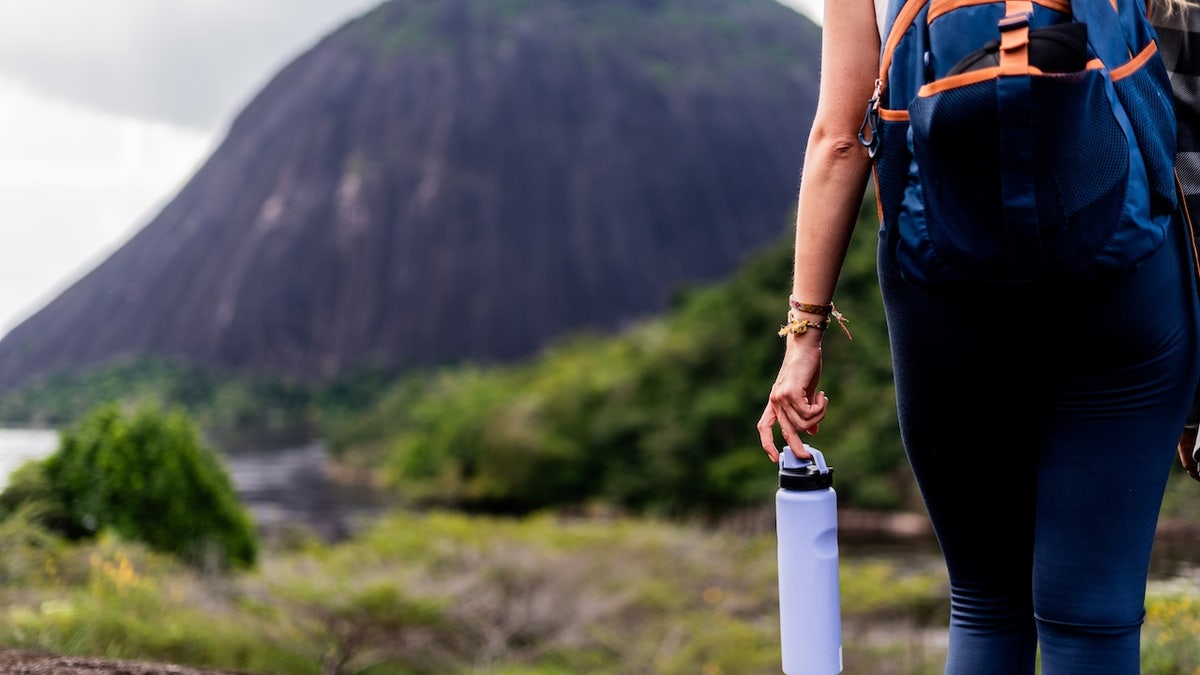Woman hiker shown from behind holding water bottle