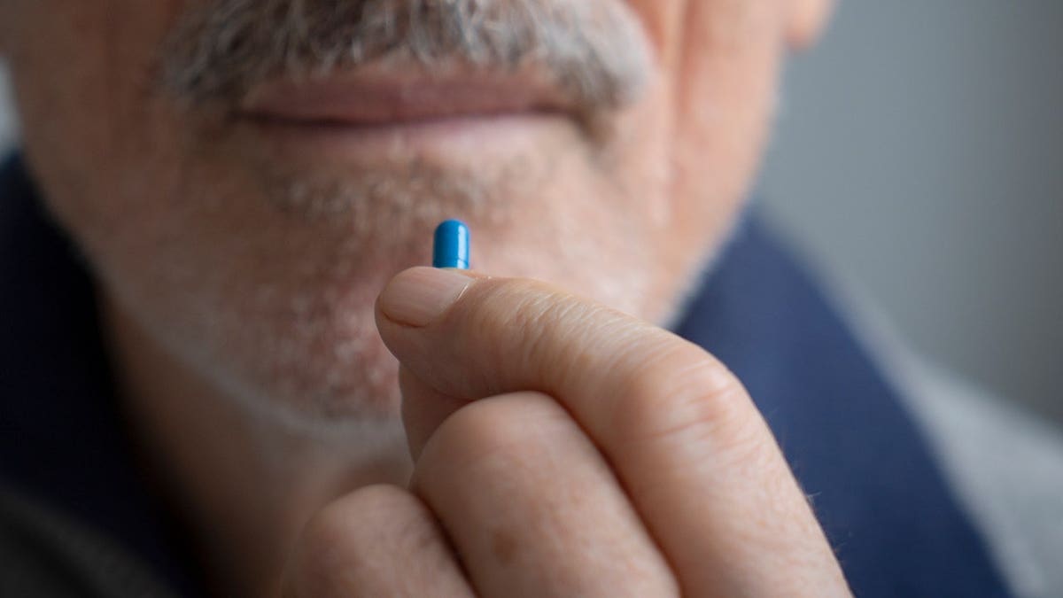 Senior man holds a pill in close-up.