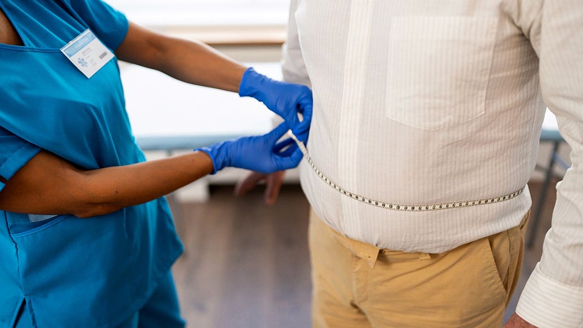Female doctor measures senior male patient's waist during annual medical checkup