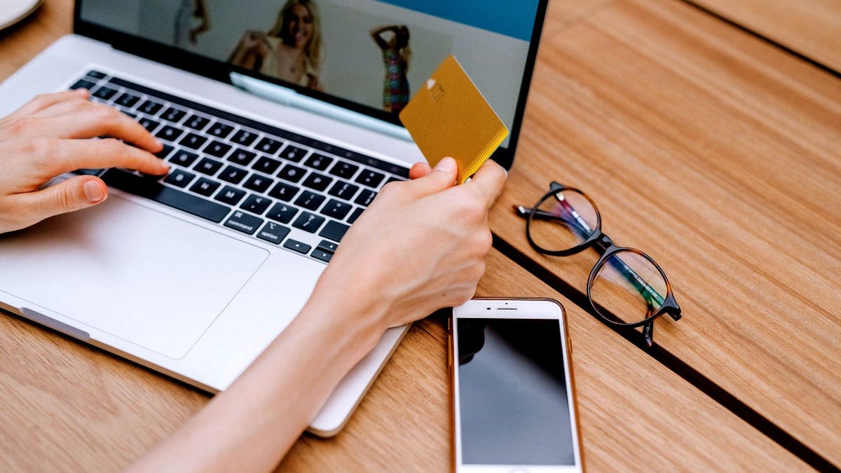 A person holds a card next to a laptop.