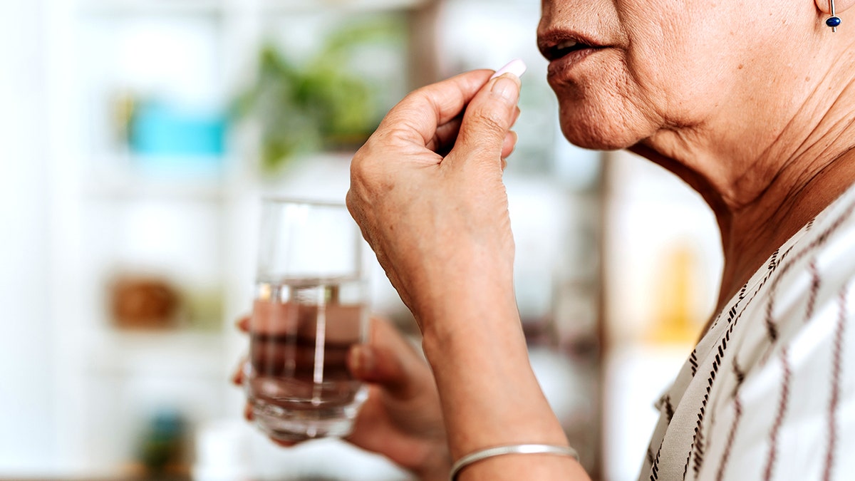 Older woman puts a pill up to her mouth while holding glass of water in other hand